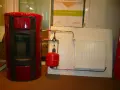 Poêle à granulé hydro rouge connecté à un radiateur blanc. Le système de chauffage est prêt.