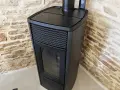 Poêle à granulés noir moderne, avec écran de contrôle, adossé à un mur de pierres. Apprenez comment éteindre un poêle à granulé en toute sécurité.