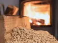 Un tronc de bois et des granulés attendent le tirage poêle à bois. Le feu crépite dans le foyer en arrière-plan.