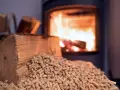 Un poêle à bois Prime Renov crache des flammes chaleureuses. Devant, une bûche et des granulés de bois attendent d'être utilisés.