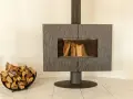 Un poêle moderne avec une cheminée vitrée et du bois de chauffage dans un panier. La **déco derrière un poêle** est sobre, mettant en valeur l'âtre.
