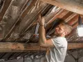 Un homme pose une isolation réfléchissante sous les chevrons. Il utilise une agrafeuse pour fixer le matériau. Ce chantier pourrait être éligible à un pret travaux CAF.