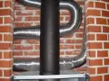 Mur brique réfractaire derrière poêle, avec conduits métalliques flexibles.