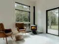Un poêle à granule appartement, avec deux fauteuils en cuir marron et une vue sur la forêt.