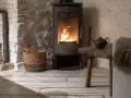 Poêle à bois moderne avec feu allumé, panier de bois, table rustique et miroir ancien.