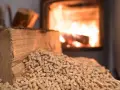 Un poêle à granulés en marche, avec des bûches et des granulés de bois à proximité. La question "peut on recharger un poêle à granulés en marche" est soulevée.