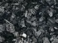 Gros plan sur des morceaux de machefer pellet, résidus noirs et gris de combustion, évoquant la chaleur d'un feu de bois.