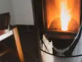 Flammes vives dans un poêle à granulés couleur cendre. Un sac en papier est visible en bas, prêt à être utilisé.