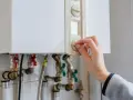 Main tenant ajuste le thermostat de sa chaudière à gaz. Une aide pour le changement de chaudière gaz est peut-être nécessaire.