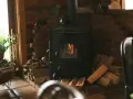 Poêle à bois avec arrivée d'air extérieur, crépitant joyeusement dans un coin cosy, entouré de bois prêt à chauffer.