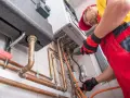 Un technicien installe une chaudière à gaz, une étape clé pour ma prime rénov. Il manipule des tuyaux en cuivre avec soin.