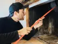 Ramoneur au visage barbouillé de suie utilise une brosse pour nettoyer le conduit d'un poêle à bois, assurant le bon fonctionnement du deflecteur poele a bois.