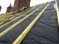 Charpente de toiture avec isolant noir et liteaux en bois, près de cheminées en brique.