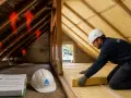 Un ouvrier installe une isolation dans un grenier. Les flèches rouges indiquent la perte de chaleur. Découvrez le prix de l'isolation des combles pour un meilleur confort.