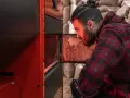 Homme vérifiant un poêle à granulés, peut-être une alarme 6 s'est déclenchée. Sacs de granulés en arrière-plan.