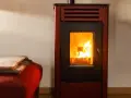 Poêle à bois avec soufflerie, ses flammes dansent joyeusement, réchauffant la pièce. Une couverture douillette est posée sur un fauteuil rouge à proximité.