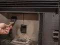 Main d'une personne nettoyant la chambre de combustion d'un poêle à pellet MCZ avec une brosse. Un problème de nettoyage peut causer des dysfonctionnements.