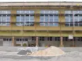 Bâtiment en rénovation énergétique, échafaudages et isolation jaune recouvrent la façade. Des tas de sable et de gravier sont prêts pour les travaux.
