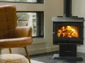 Un confortable fauteuil en cuir brun fait face à un poêle à bois non étanche, où des flammes dansent joyeusement dans le foyer.