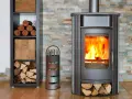 Poêle moderne avec un feu vif, entouré de bois de chauffage et de pellets rangés dans une étagère.