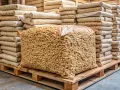 Une palette de bois supporte un grand sac transparent rempli de granulés de bois, entouré de piles de sacs plus petits. Combien de sac de granulés sur une palette ?