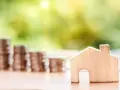 Une petite maison en bois et des piles de pièces de monnaie suggèrent un coup de pouce pour quel groupe : les investisseurs immobiliers.
