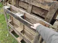 Maintenant, la question se pose : peut-on brûler du bois de palette dans une cheminée ? Une main touche des palettes en bois usagées, empilées sur de l'herbe.