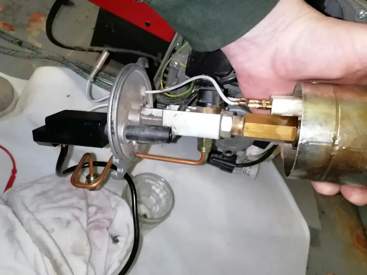 Main d'un technicien ajustant un composant de chaudière fioul en sécurité. Tuyaux en cuivre et raccords laiton visibles.