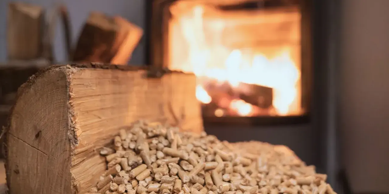 Un tronc de bois et des granulés attendent le tirage poêle à bois. Le feu crépite dans le foyer en arrière-plan.