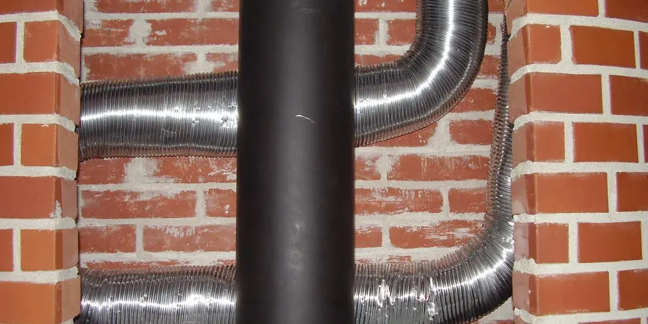 Mur brique réfractaire derrière poêle, avec conduits métalliques flexibles.