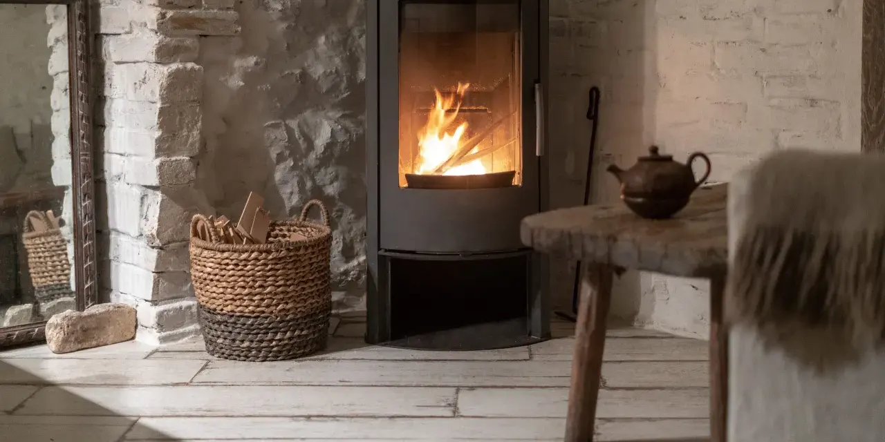 Poêle à bois moderne avec feu allumé, panier de bois, table rustique et miroir ancien.