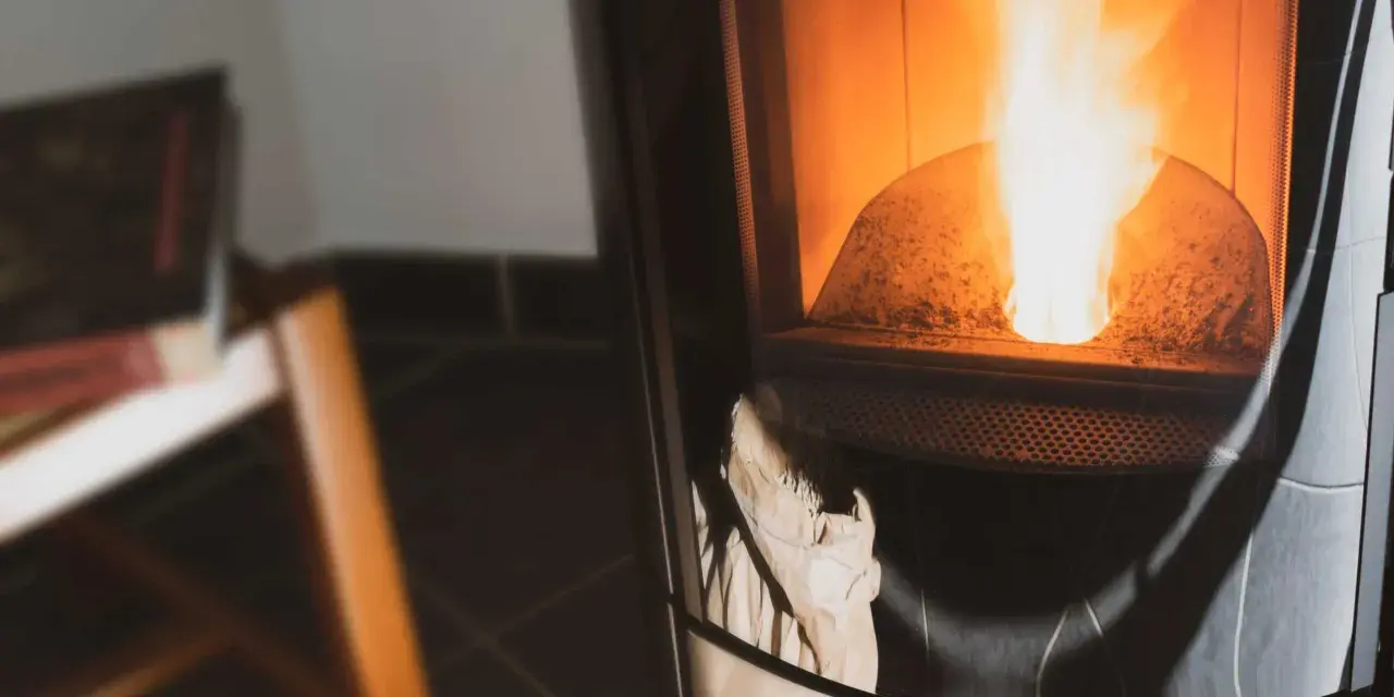 Flammes vives dans un poêle à granulés couleur cendre. Un sac en papier est visible en bas, prêt à être utilisé.
