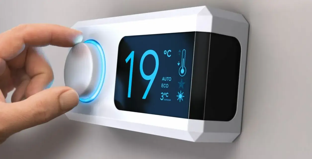 Main d'une personne ajustant le réglage de température sur un cee thermostat connecté affichant 19°C.
