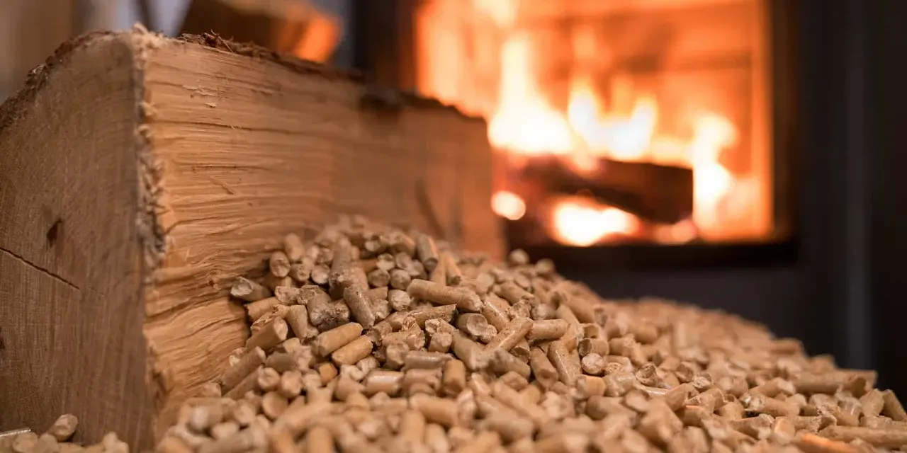 Bûches et granulés de bois, prêts pour une chaudière bois mixte. Le feu crépite en arrière-plan.