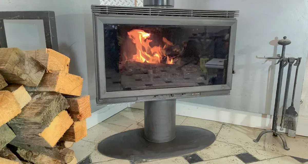 Un poêle à bois avec une vitre propre pour changer une vitre de poele a bois. Des bûches de bois sont empilées à gauche.