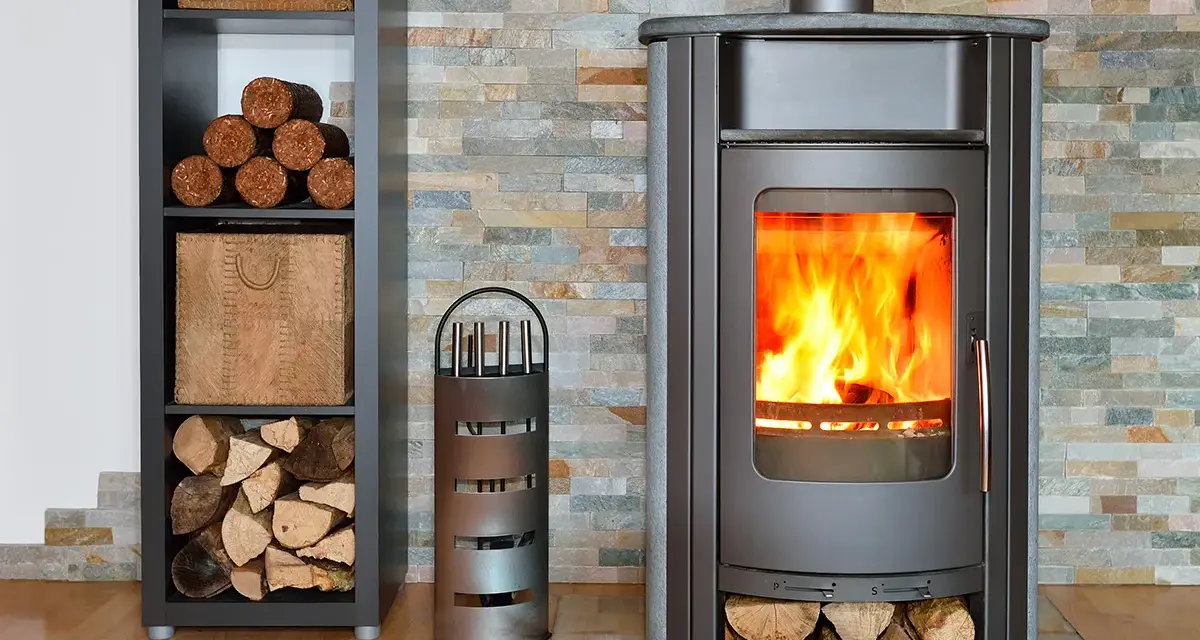 Poêle moderne avec un feu vif, entouré de bois de chauffage et de pellets rangés dans une étagère.