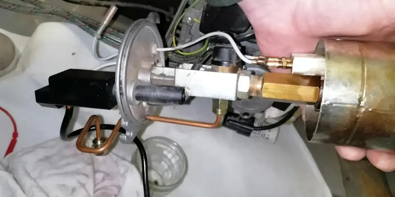 Main d'un technicien ajustant un composant de chaudière fioul en sécurité. Tuyaux en cuivre et raccords laiton visibles.