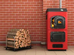 Une chaudière biomasse rouge flamboyante, avec une porte ouverte révélant des flammes vives, est prête à chauffer une maison. À côté, une pile de bois de chauffage attend patiemment.