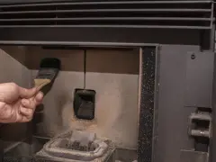 Main d'une personne nettoyant la chambre de combustion d'un poêle à pellet MCZ avec une brosse. Un problème de nettoyage peut causer des dysfonctionnements.