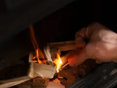 Main allumant un feu dans un poêle à bois avec une allumette.