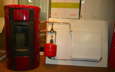 Poêle à granulé hydro rouge connecté à un radiateur blanc. Le système de chauffage est prêt.
