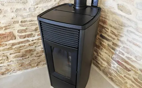 Poêle à granulés noir moderne, avec écran de contrôle, adossé à un mur de pierres. Apprenez comment éteindre un poêle à granulé en toute sécurité.