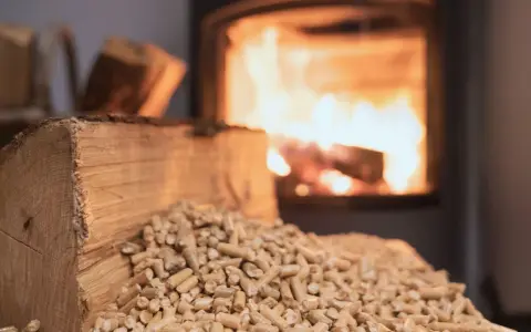 Un tronc de bois et des granulés attendent le tirage poêle à bois. Le feu crépite dans le foyer en arrière-plan.