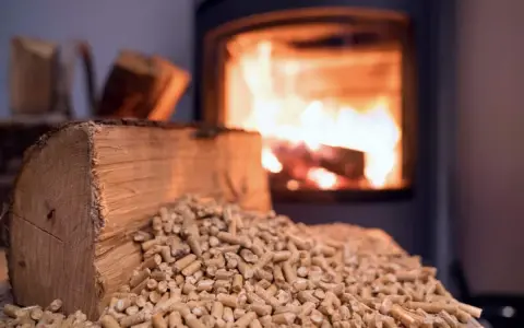 Un poêle à bois Prime Renov crache des flammes chaleureuses. Devant, une bûche et des granulés de bois attendent d'être utilisés.