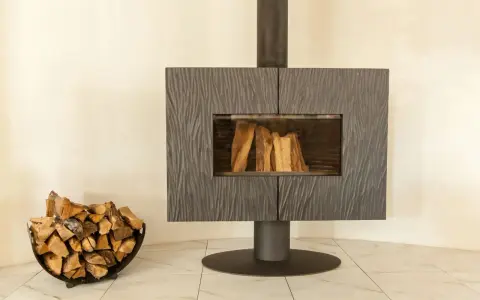 Un poêle moderne avec une cheminée vitrée et du bois de chauffage dans un panier. La **déco derrière un poêle** est sobre, mettant en valeur l'âtre.