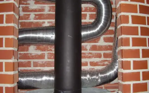 Mur brique réfractaire derrière poêle, avec conduits métalliques flexibles.