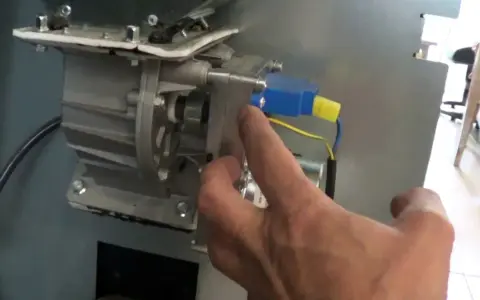 Main d'un homme manipulant le mécanisme d'un poêle à granulés, pour nettoyer le pressostat.