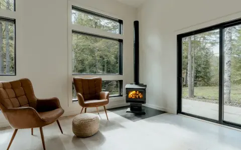 Un poêle à granule appartement, avec deux fauteuils en cuir marron et une vue sur la forêt.