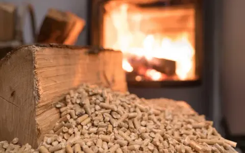 Un poêle à granulés en marche, avec des bûches et des granulés de bois à proximité. La question "peut on recharger un poêle à granulés en marche" est soulevée.