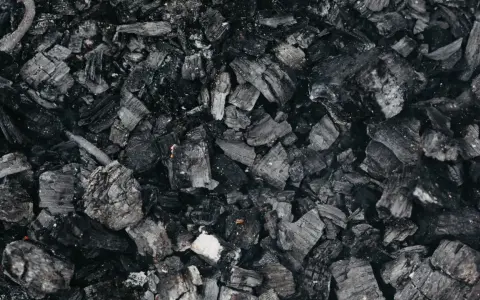 Gros plan sur des morceaux de machefer pellet, résidus noirs et gris de combustion, évoquant la chaleur d'un feu de bois.